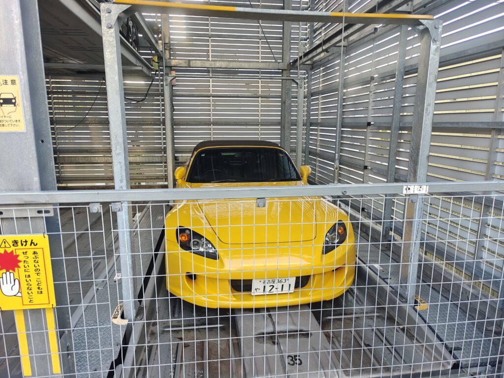 立体駐車場のパレットに収まる黄色いホンダ・S2000のフロントビュー