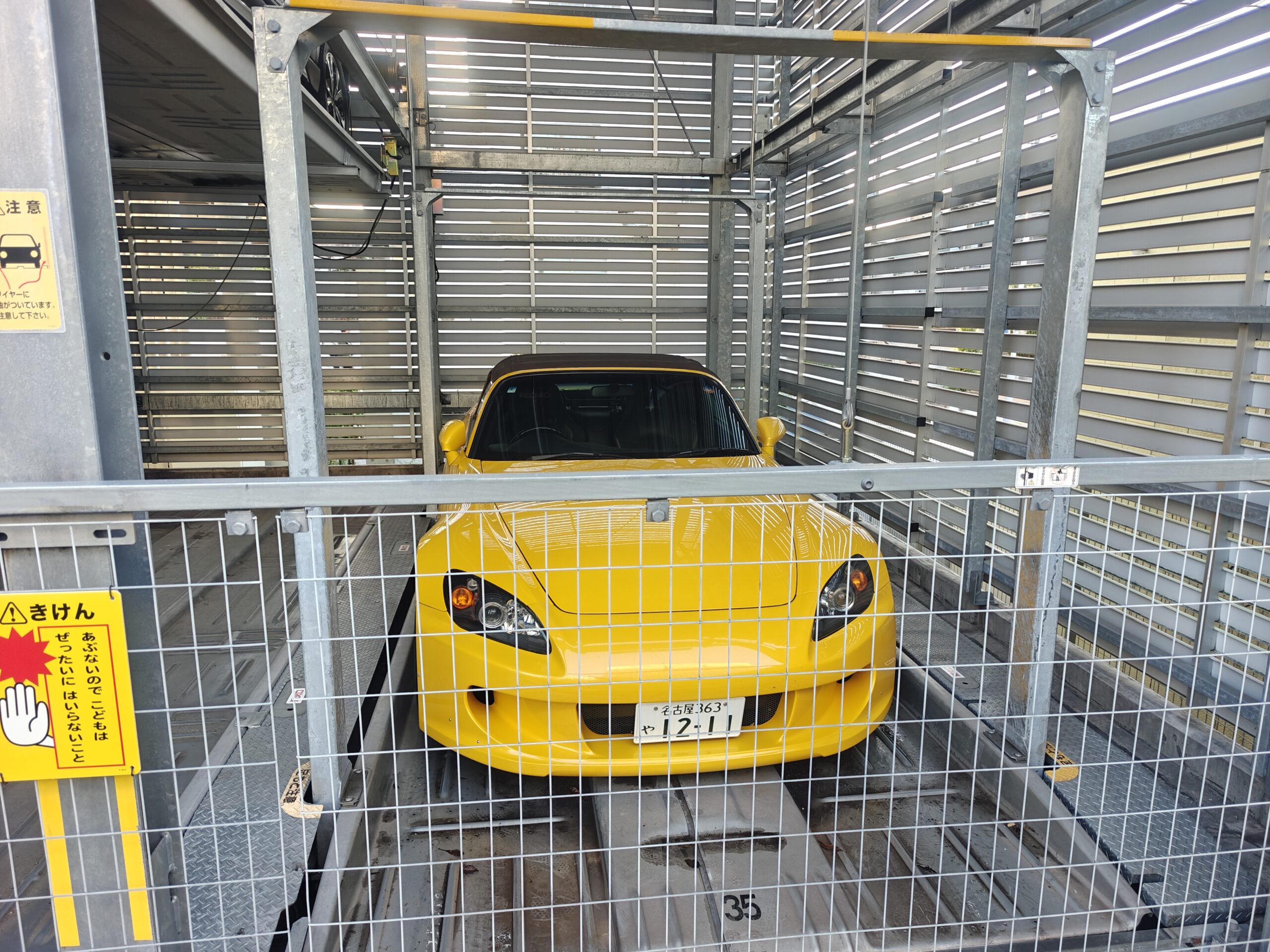 立体駐車場のパレットに収まる黄色いホンダ・S2000のフロントビュー